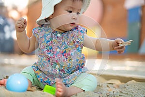 Adorable 9 months old baby playing outdoors - lifestyle portrait of mixed ethnicity Asian Caucasian baby girl playing with block