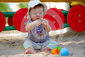 Adorable 9 months old baby playing outdoors - lifestyle portrait of mixed ethnicity Asian Caucasian baby girl playing with block