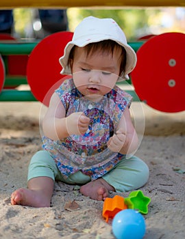 Adorable 9 months old baby playing outdoors - lifestyle portrait of mixed ethnicity Asian Caucasian baby girl playing with block