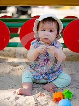 Adorable 9 months old baby playing outdoors - lifestyle portrait of mixed ethnicity Asian Caucasian baby girl playing with block