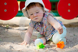 Adorable 9 months old baby playing outdoors - lifestyle portrait of mixed ethnicity Asian Caucasian baby girl playing with block