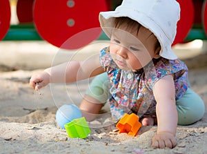 Adorable 9 months old baby playing outdoors - lifestyle portrait of mixed ethnicity Asian Caucasian baby girl playing with block