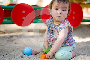 Adorable 9 months old baby playing outdoors - lifestyle portrait of mixed ethnicity Asian Caucasian baby girl playing with block