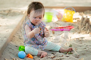 Adorable 9 months old baby playing outdoors - lifestyle portrait of mixed ethnicity Asian Caucasian baby girl playing with block