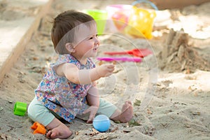 Adorable 9 months old baby playing outdoors - lifestyle portrait of mixed ethnicity Asian Caucasian baby girl playing with block