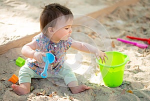 Adorable 9 months old baby playing outdoors - lifestyle portrait of mixed ethnicity Asian Caucasian baby girl playing with block