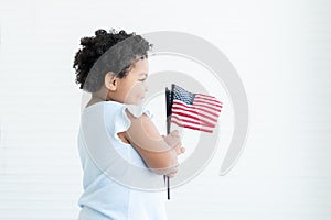 Adorable African American chubby kid girl smiling standing and holding small USA flags in hand at home. Celebrating 4th July