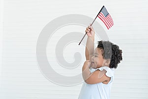 Adorable African American chubby kid girl smiling standing and holding small USA flags in hand at home. Celebrating 4th July