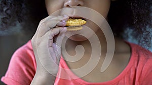 Adorable African-American girl biting sweet cookie, unhealthy nutrition close-up