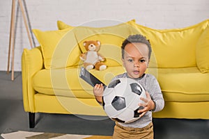 adorable african american toddler holding soccer ball and remote controller