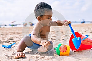 Adorable african american toddler playing with toys sitting on the sand at the beach