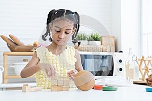 Adorable African little child girl concentrate playing wooden blocks toy and colorful pyramid puzzle in kitchen at home. Education