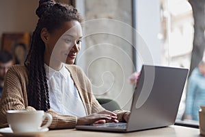 Adorable African woman student types text on laptop keyboard, works, studies, doing research or prepares for exam online