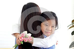 Adorable Asia happy smiling daughter girl giving beautiful tulip flowers for her mother and hugging her mom with love, warm love