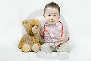 Adorable asian baby boy in pink shirt plays in doctor toy bear and red stethoscope.Health care and medical concept.