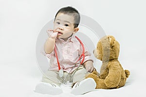 Adorable asian baby boy in pink shirt plays in doctor toy bear and red stethoscope.Health care and medical concept
