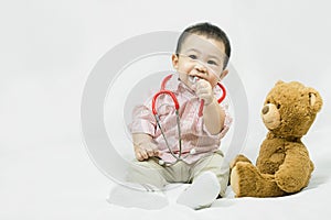 Adorable asian baby boy in pink shirt plays in doctor toy bear and red stethoscope.Health care and medical concept