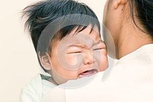 Adorable asian baby sick and crying on mom shoulder.