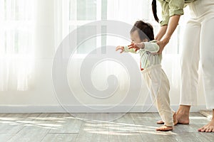 Adorable Asian baby toddler learning to walk with mom helping at home. Little baby boy looking in front to walking step by step