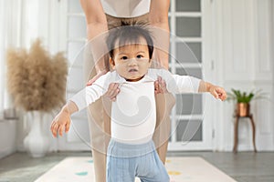 Adorable Asian baby toddler learning to walk with mom helping at home. Little baby boy looking in front to walking step by step