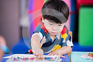 Adorable Asian boy reached for pick up chalk paint, baby made art on the paper placed on the table. Child learn crafts at home.