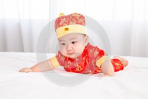 Adorable Asian boy in red Chinese Costume clothes lie on the stomach try crawling on white bed, cute innocent infant baby start
