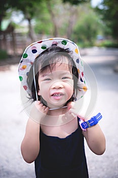 Adorable Asian child kid girl stand on the road in the afternoon heat. She is wearing a colorful polka dot hat with a sweet smiley