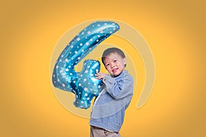 Adorable Asian four year old boy celebrating his birthday holding number 4 blue balloon on orange colored background with clipping