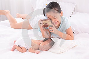 Adorable Asian girl enjoy playing wooden camera taking photo newborn infant while sleeping, lovely relationship childhood sibling