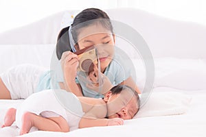 Adorable Asian girl enjoy playing wooden camera taking photo newborn infant while sleeping, lovely relationship childhood sibling