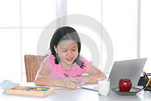 Adorable Asian girl happy learning online with technology laptop on desk at home, school girl typing answer or response with