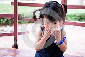 Adorable Asian girl was sitting and eating a white bread sandwich deliciously. Children eat snacks.