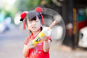 Adorable Asian girl wearing red Chinese New Year dress. Children play with yellow vintage umbrella.