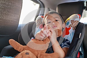 Adorable Asian kid boy Toddler age 1-year-old Protection Sitting in the Car Seat with Safety Belt Locked and Holding Bear Doll