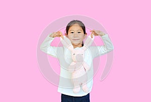 Adorable asian kid girl holding ears of pink rabbit doll isolated on pink background. Happy child on Easter