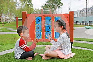 Adorable Asian little boy and young girl kid sitting in the garden playground with playing rock scissors paper game