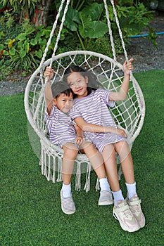 Adorable Asian little boy and young girl kid sitting together on the white cradle or swing in the garden