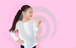 Adorable asian little child girl looking with thumb pointing beside with smiling on pink background with copy space