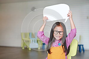 Adorable Asian little girl holding empty blank speech bubble to say something in the classroom with smiling and looking straight