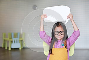 Adorable Asian little girl holding empty blank speech bubble to say something in the classroom with smiling and looking straight