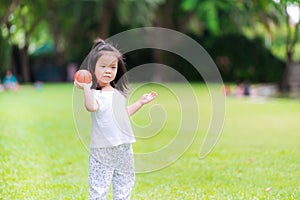 Adorable Asian little girl playing in the green lawn in the public park throwing orange ball similar to a little basketball.