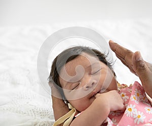 Adorable Asian newborn baby girl sleeping on father hand and sucking her thumb. Dad nursing his infant with love on bed at home.