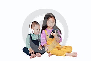 Adorable Asian older sister and little brother sharing to enjoys listening music with headphones by smartphone isolated over white