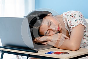 Adorable Asian woman falling asleep on the arm on table in front of a laptop computer after a tiring day photo