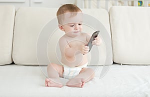 Adorable baby boy in diapers sitting on sofa and using smartphone