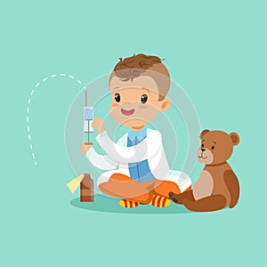 Adorable baby boy dressed as a doctor playing with teddy bear toy. Kid preparing syringe for his sick patient