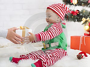 Adorable baby boy in elf costume getting Christmas gift
