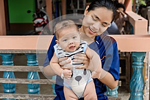 Adorable baby boy looking at camera with interest on arm of young woman.