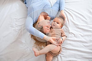 Adorable baby boy and loving blonde mother laying on bed