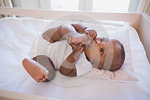 Adorable baby boy lying in his crib chewing foot photo
